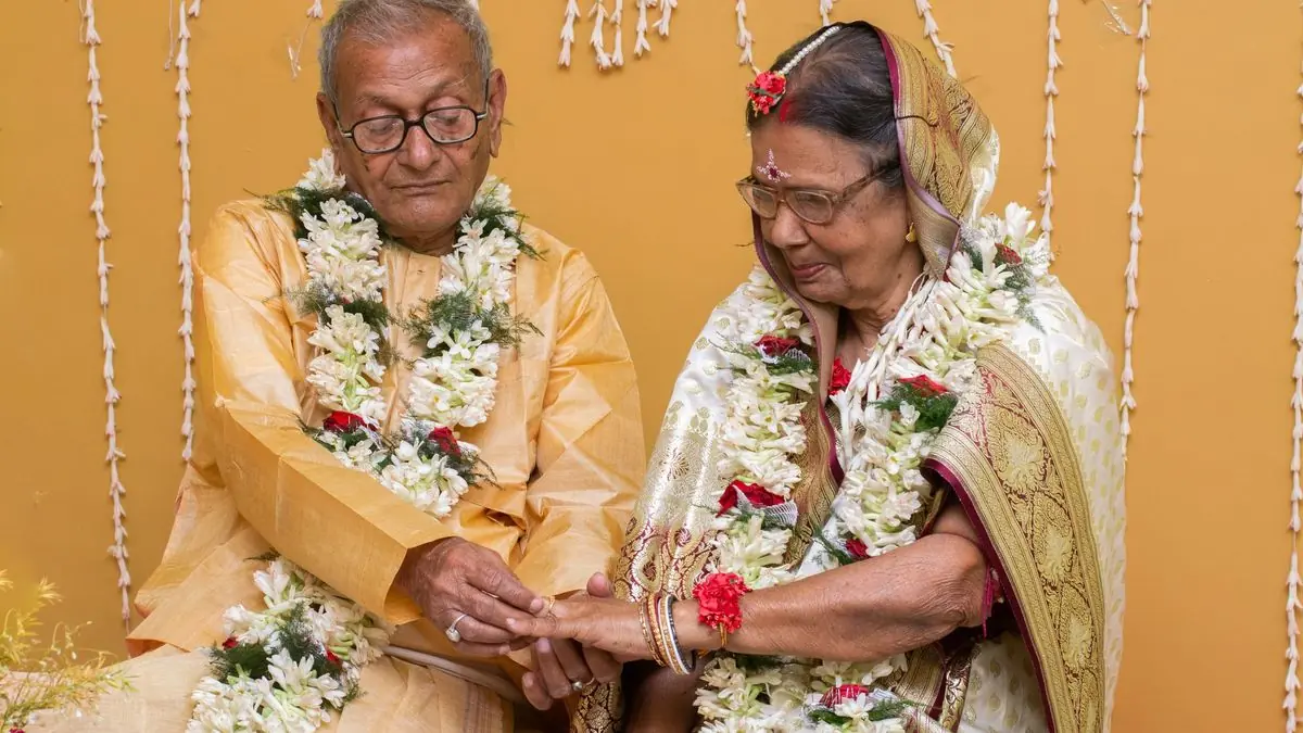 An elderly couple in garlands exchanging rings at their anniversary celebration