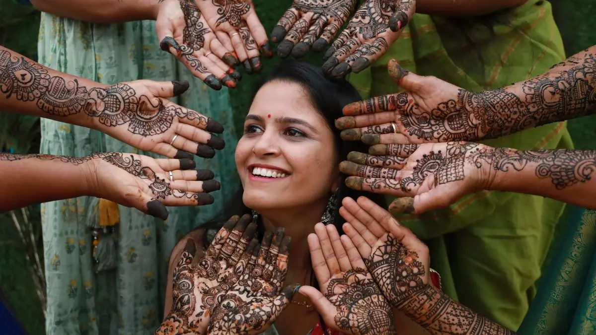 A smiling woman surrounded by hands decorated with mehndi
