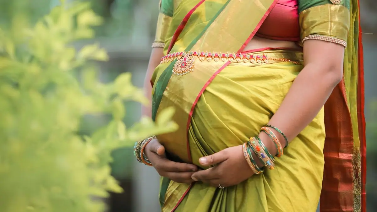 A mother-to-be in a silk saree, hands resting on her baby bump
